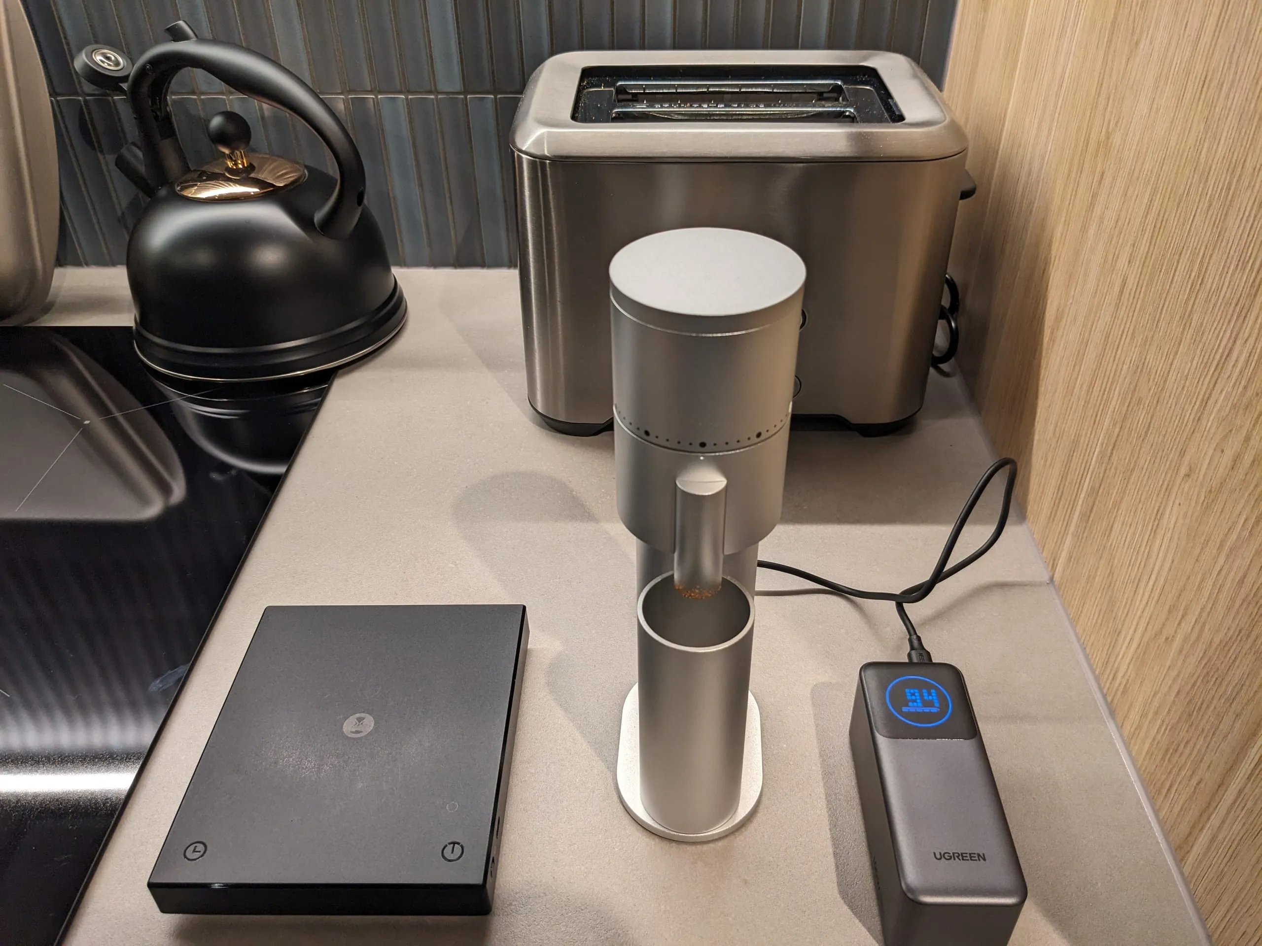 A tidy coffee corner: kettle, silver hand grinder, scales and toaster lined up on a bench.